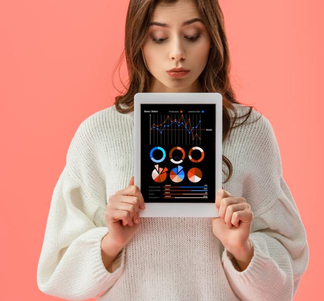 surprised young woman holding digital tablet with charts and graphs on screen isolated on pink